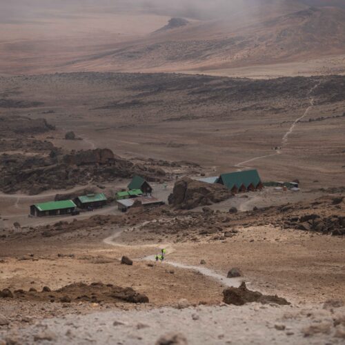 High-angle shot of hikers approaching a remote mountain base camp with rugged terrain.