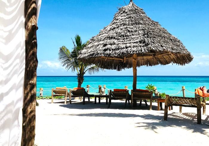 A serene tropical beach scene in Zanzibar featuring a straw umbrella and clear blue skies.