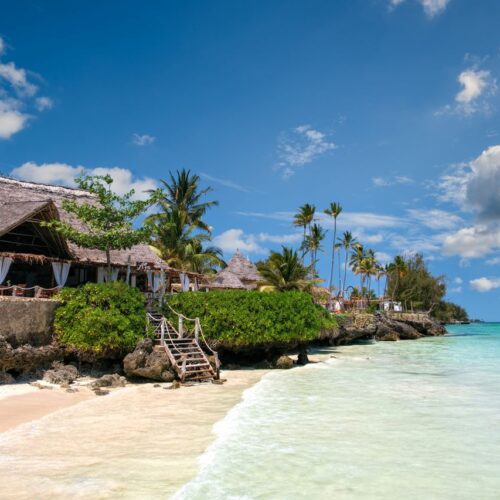 scene in Zanzibar with palm trees, turquoise sea, and a traditional villa.