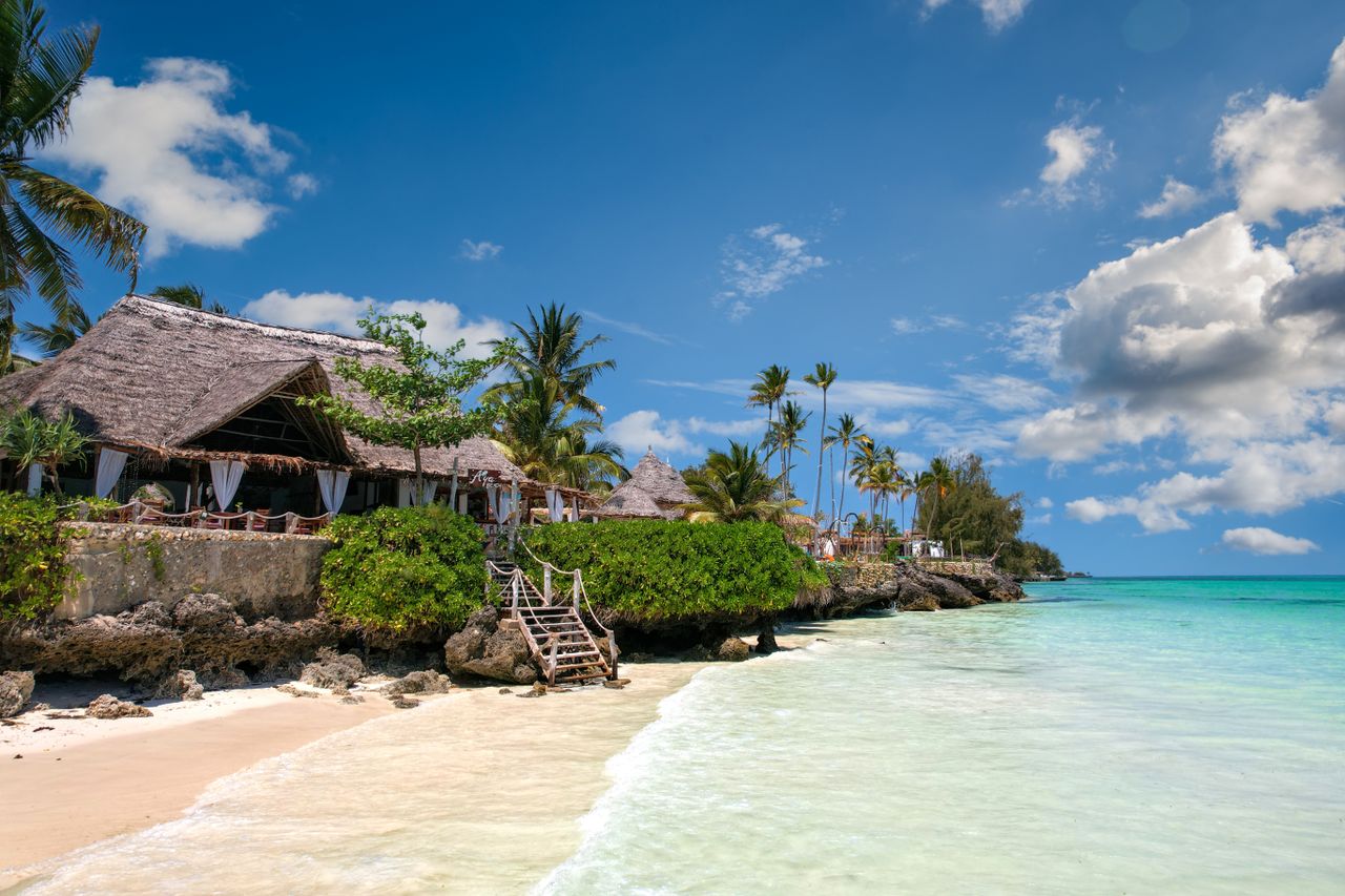 scene in Zanzibar with palm trees, turquoise sea, and a traditional villa.