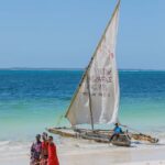 Which Tanzania Safari Is Best for You? A group of Maasai people walking by a traditional sailboat on a sunny tropical beach.
